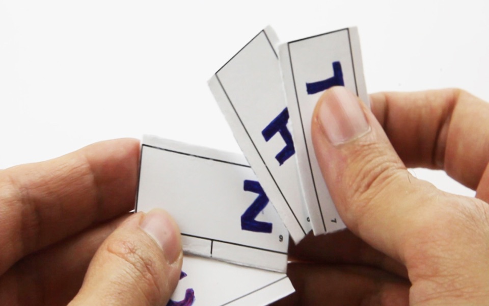 Hands holding a stack of paper pages, each marked with a letter